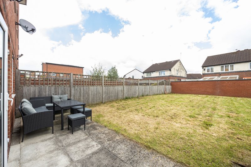 Spacious rear garden with patio seating area, wooden fence, and lawn