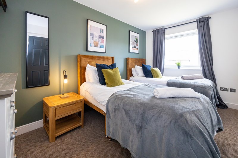 Twin bedroom with wooden headboards, grey bedding, yellow cushions and wall art