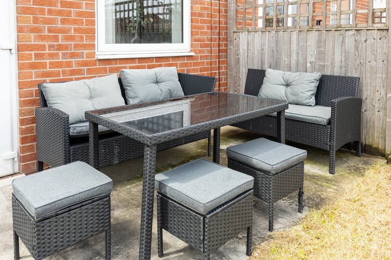 Outdoor patio seating area with rattan furniture, cushions and dining table against brick wall