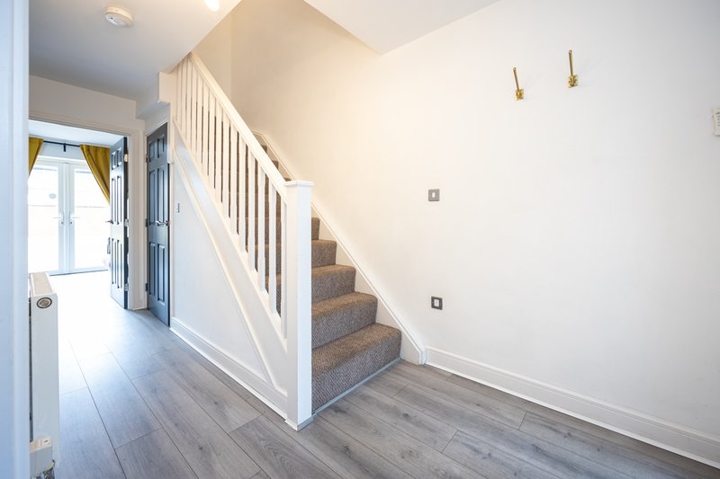 Bright hallway with wooden stairs, white railings, and laminate flooring throughout.