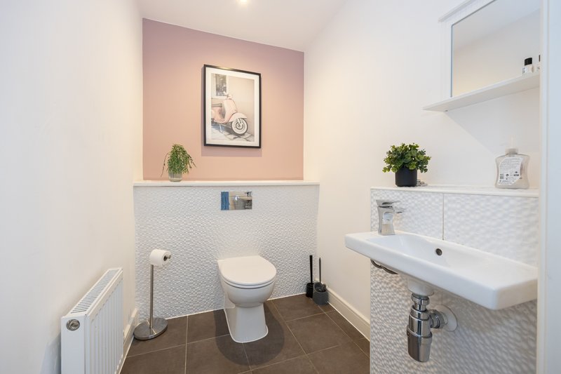 Modern bathroom with white toilet, wall-mounted sink, pink accent wall and potted plants