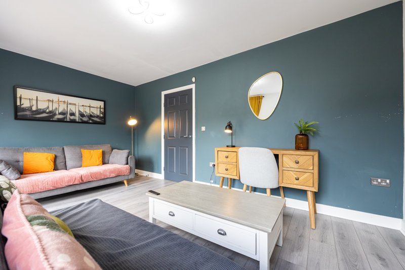 Modern bedroom with teal walls, pink sofa, wooden furniture and round mirror