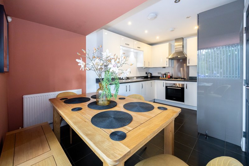 Modern kitchen with wooden dining table, white cabinetry, and pink accent wall