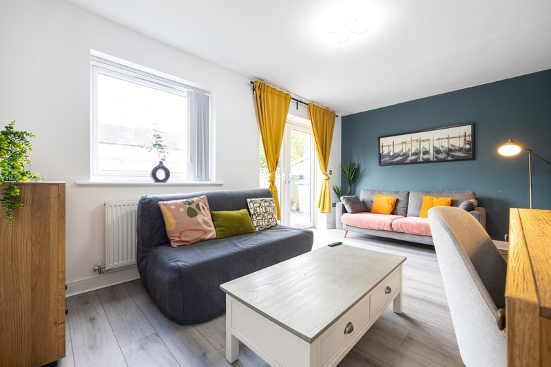 Bright living room with dark sofa, two beds, yellow curtains and teal accent wall