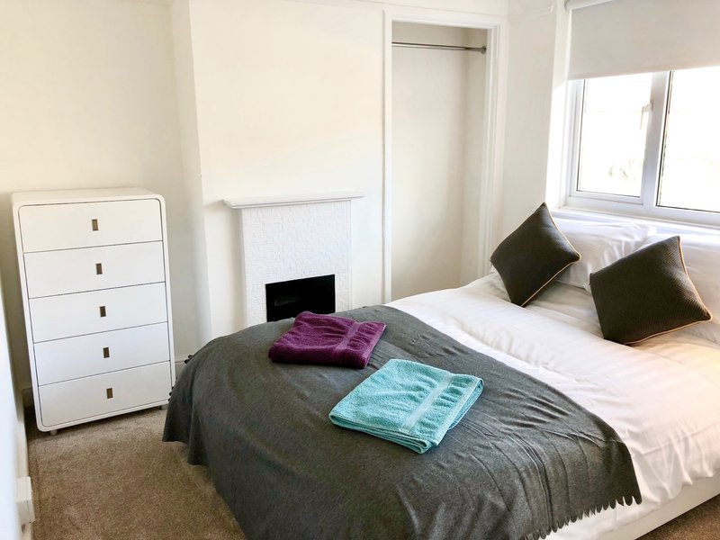Bedroom with double bed, white chest of drawers, black cushions and folded towels