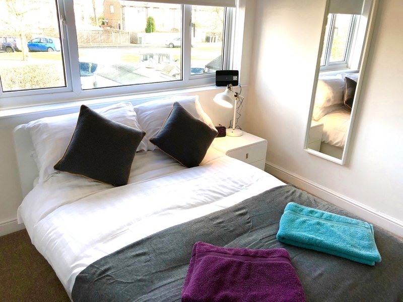 Bright bedroom with double bed, black cushions, colorful folded towels and large windows