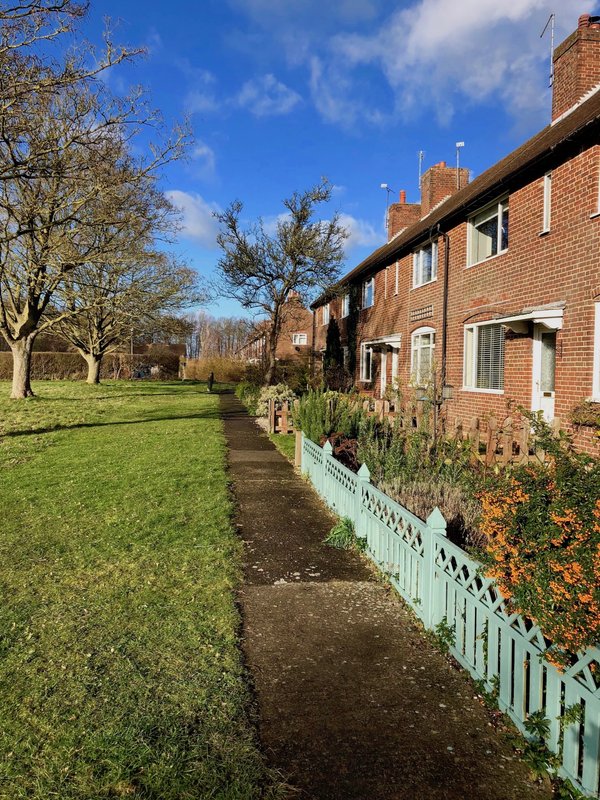 Brick terraced house with white fence, garden path and mature trees