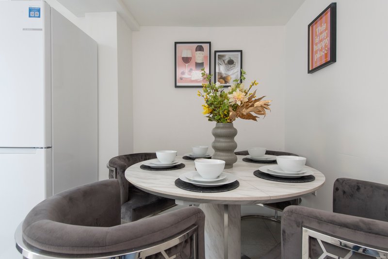 Modern dining area with round white table, grey upholstered chairs, place settings and flower arrangement