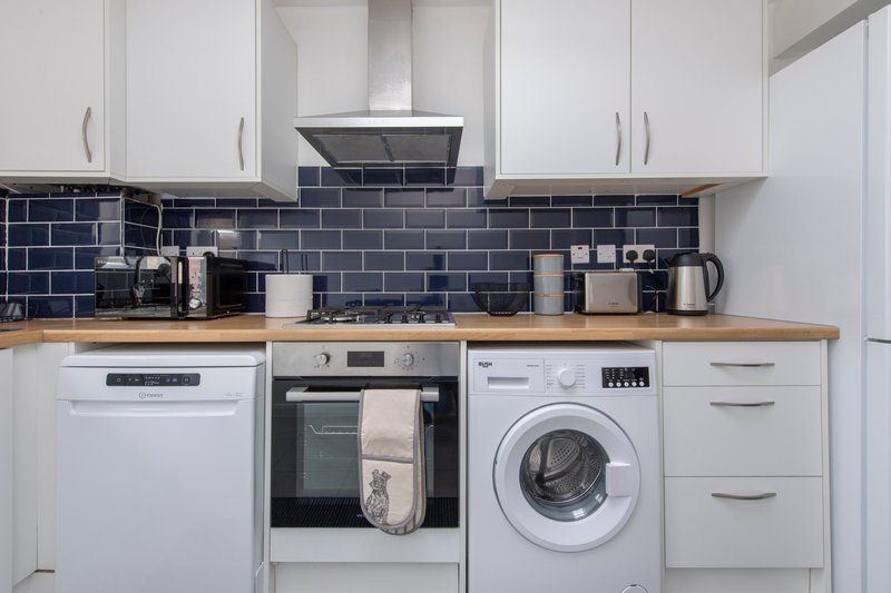 Modern white kitchen with dark tile backsplash, wooden countertop, integrated appliances and washing machine