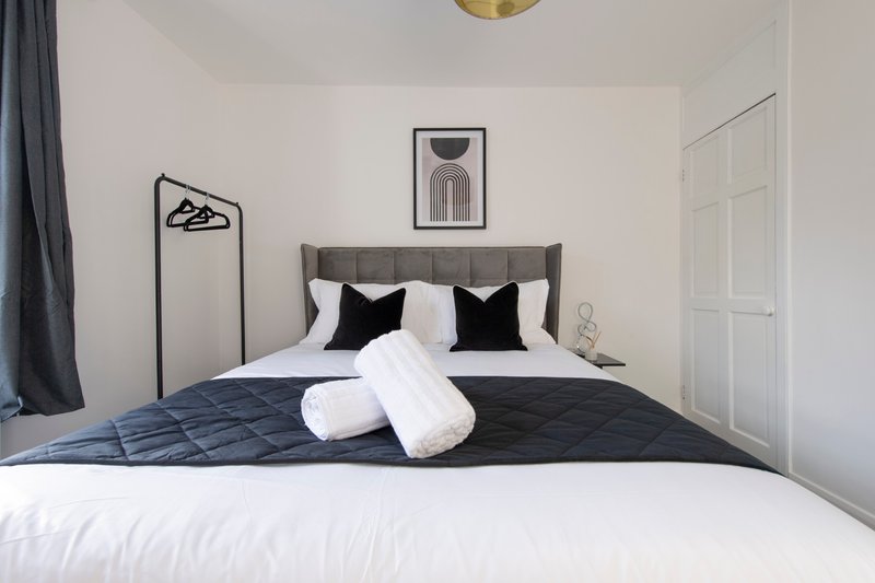 Modern bedroom with grey upholstered bed, black and white pillows, rolled towels, and minimalist wall art