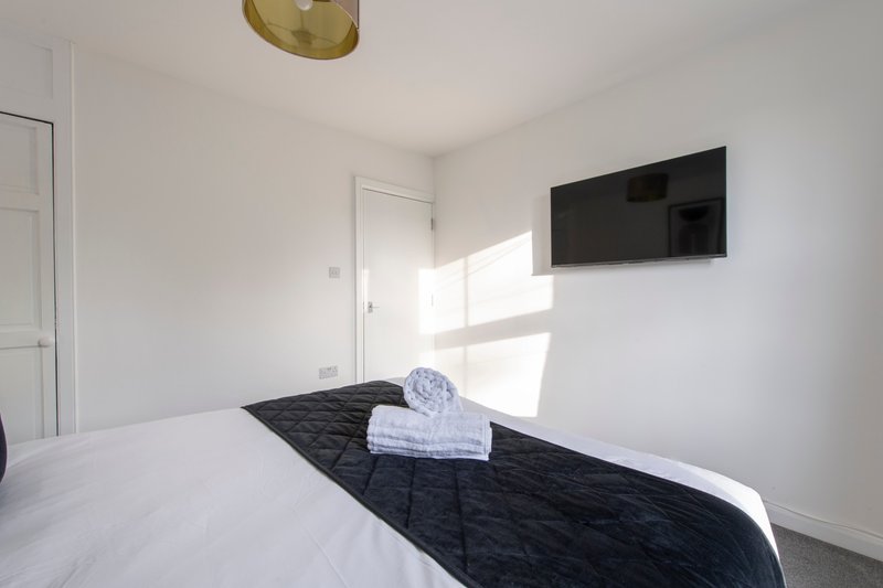 Bright modern bedroom with double bed, wall-mounted TV, and folded towels on bed runner