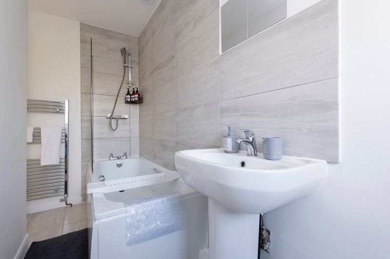 Modern bathroom with white pedestal sink, shower enclosure, heated towel rail and tiled walls