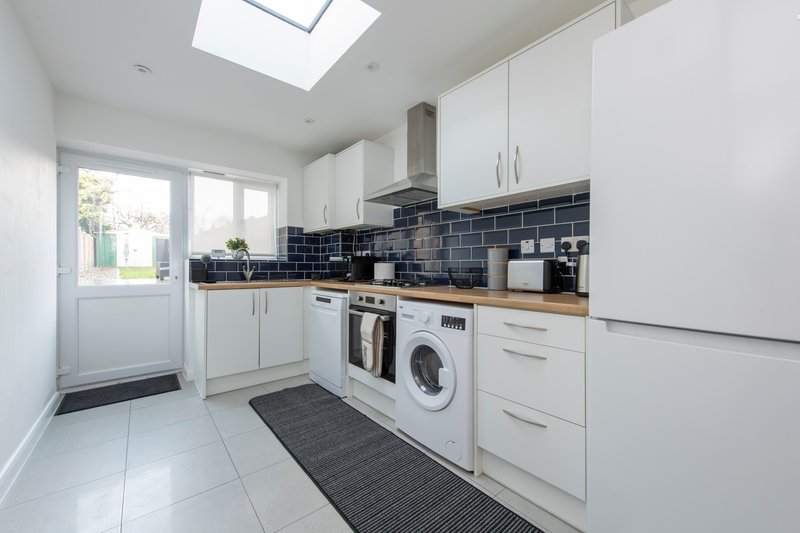 Modern kitchen with white cabinetry, dark tile backsplash, appliances and skylight