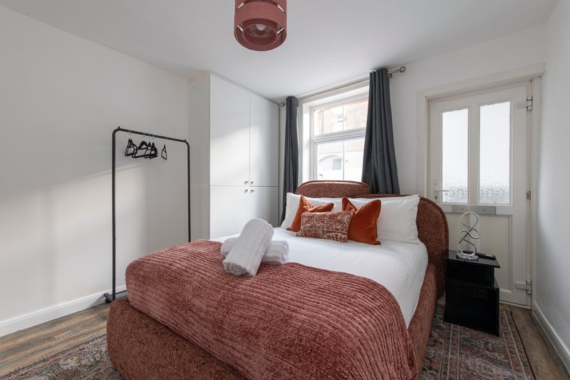 Modern bedroom with double bed, burgundy bedding, white pillows, dark curtains and wooden flooring