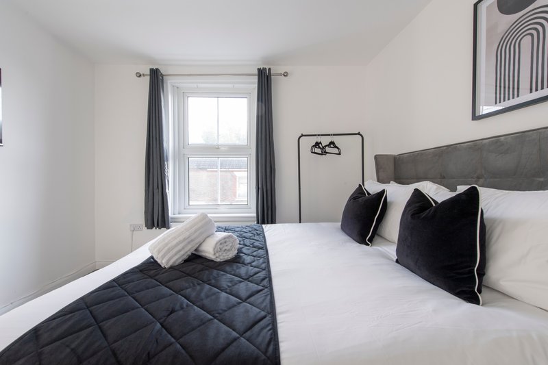 Modern bedroom with double bed, black cushions, white bedding and grey upholstered headboard