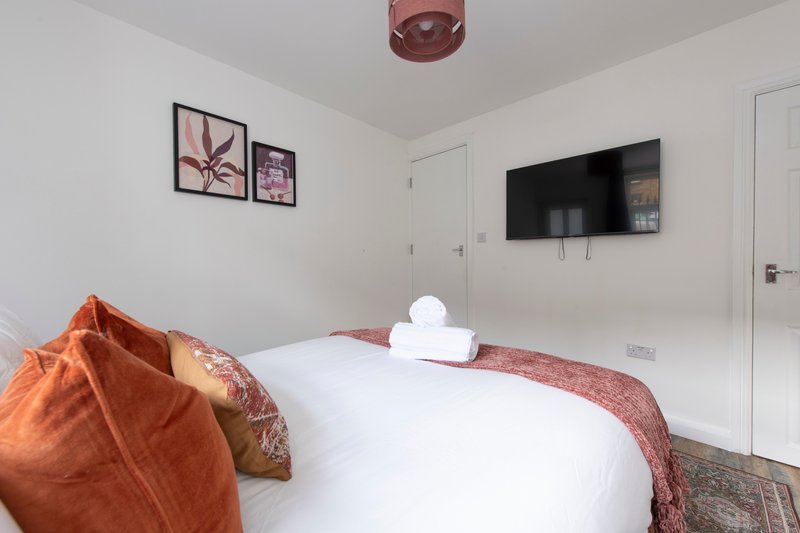 Modern bedroom with double bed, orange throw cushion, wall-mounted TV and framed wall art