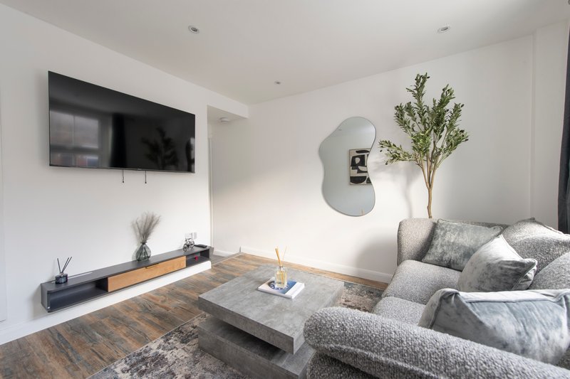 Modern living room with grey sofa, wall-mounted TV, wooden floor and potted plant