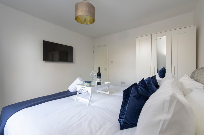 Modern bedroom with double bed, white bedding, blue cushions, wall-mounted TV and pendant light