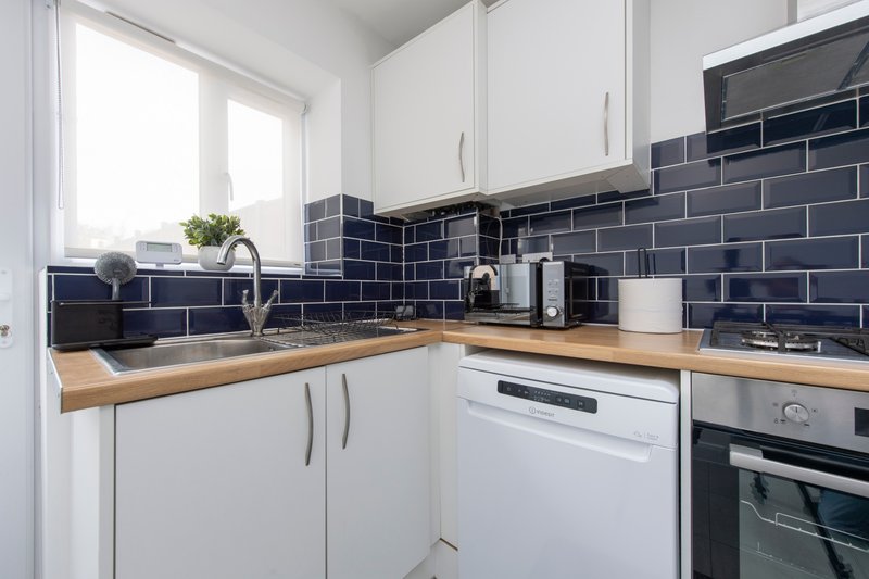 Modern kitchen with white cabinets, wooden countertop, navy subway tile backsplash and stainless steel appliances