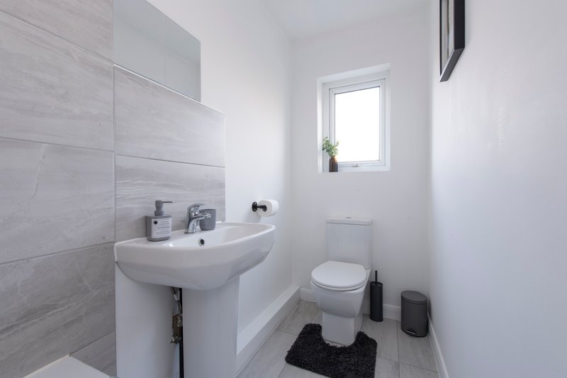 Modern bathroom with pedestal sink, toilet, gray tile wall and small window