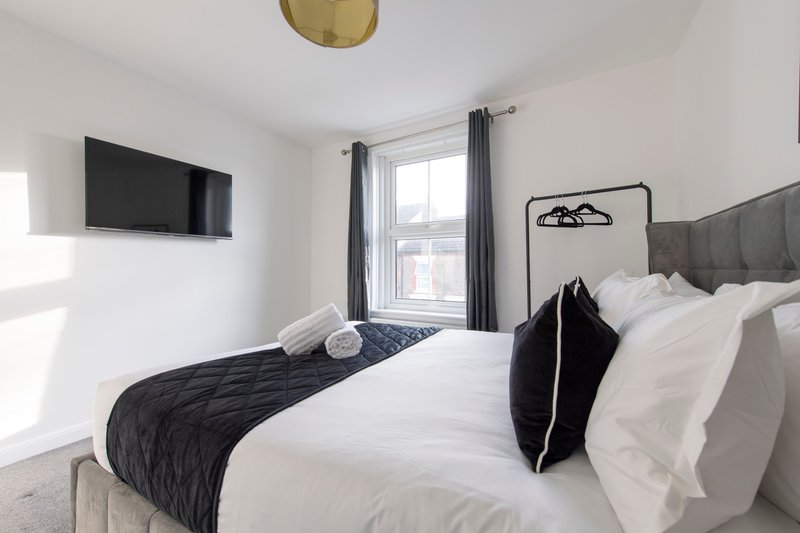 Modern bedroom with double bed, white bedding, black throw, wall-mounted TV and window