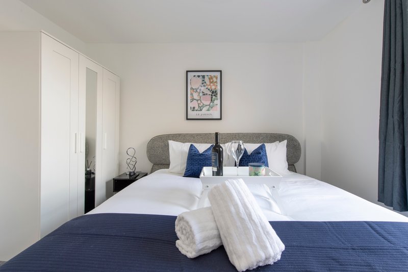 Modern bedroom with double bed, blue bedding, decorative pillows and rolled towels