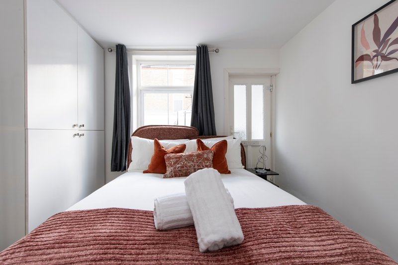 Modern bedroom with double bed, red bedding, white pillows, and large window with dark curtains