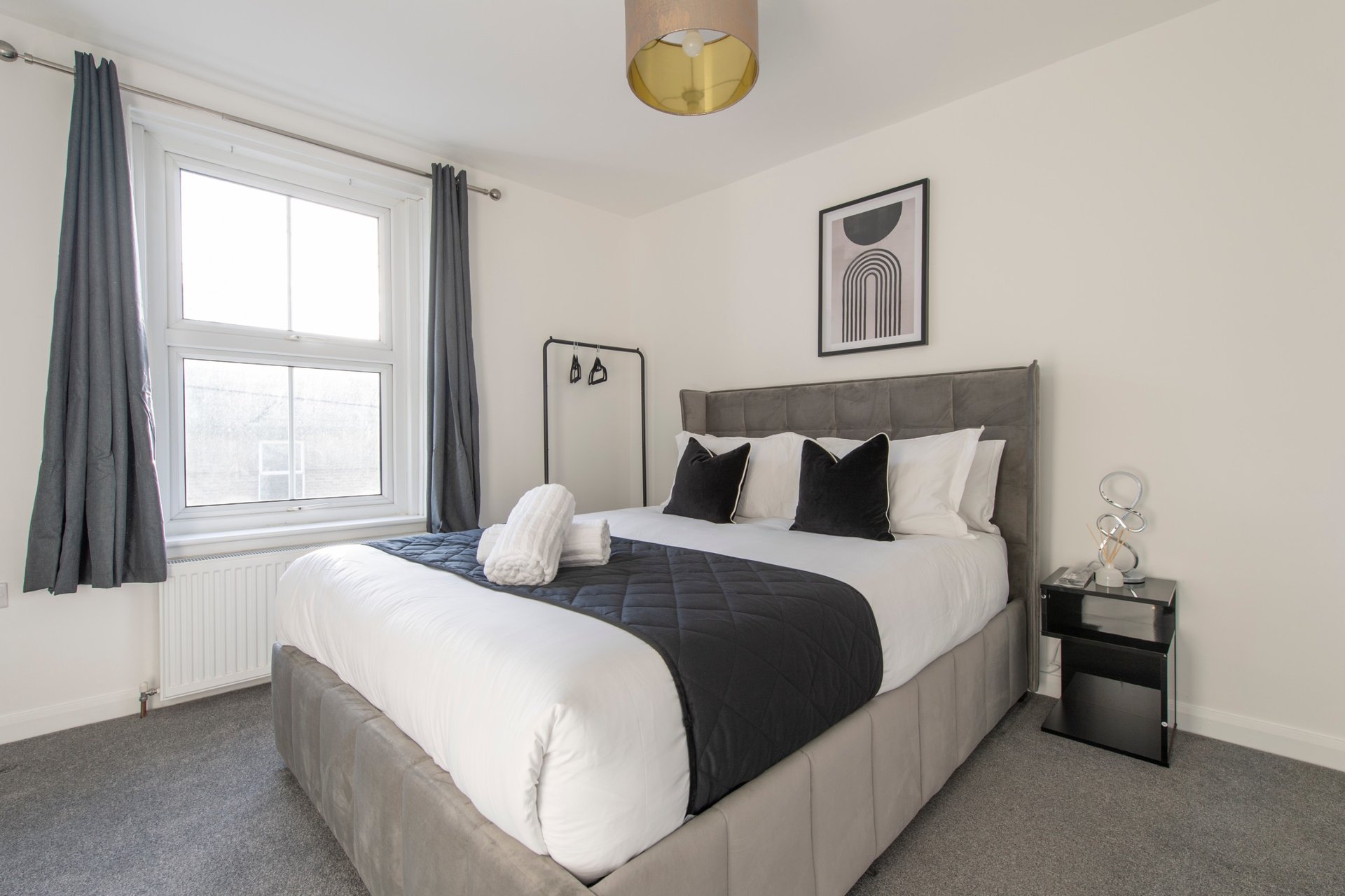 Modern bedroom with grey upholstered bed, white bedding, black accent pillows, and gold ceiling light
