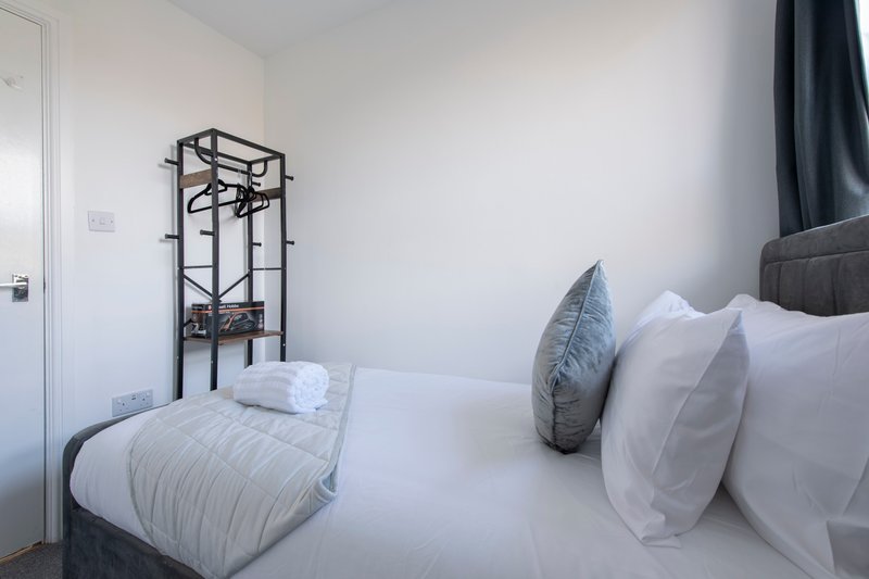 Modern bedroom with double bed, white bedding, grey pillows and metal coat stand