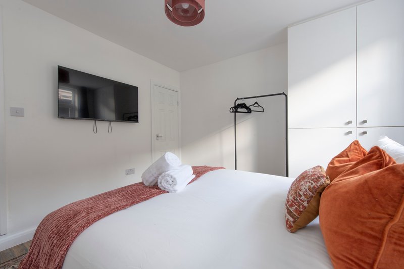Modern bedroom with double bed, white pillows, orange cushions and wall-mounted TV