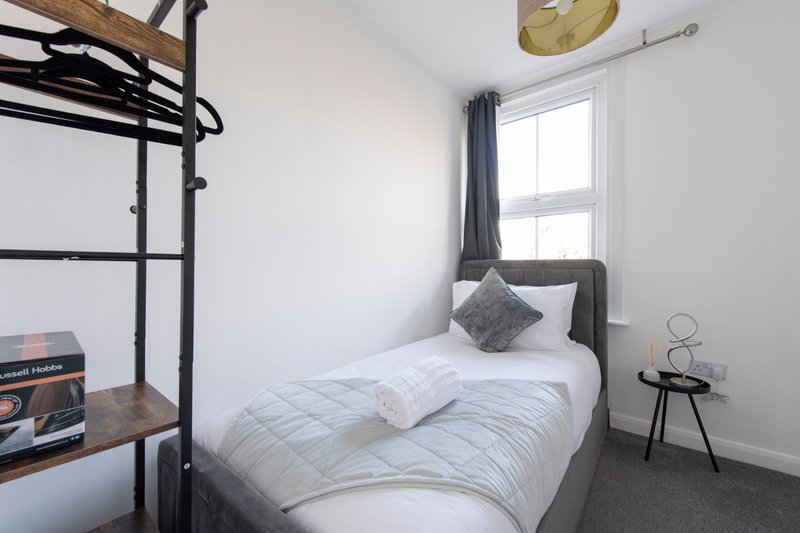 Compact bedroom with single bed, metal bunk frame, small side table and window with curtains