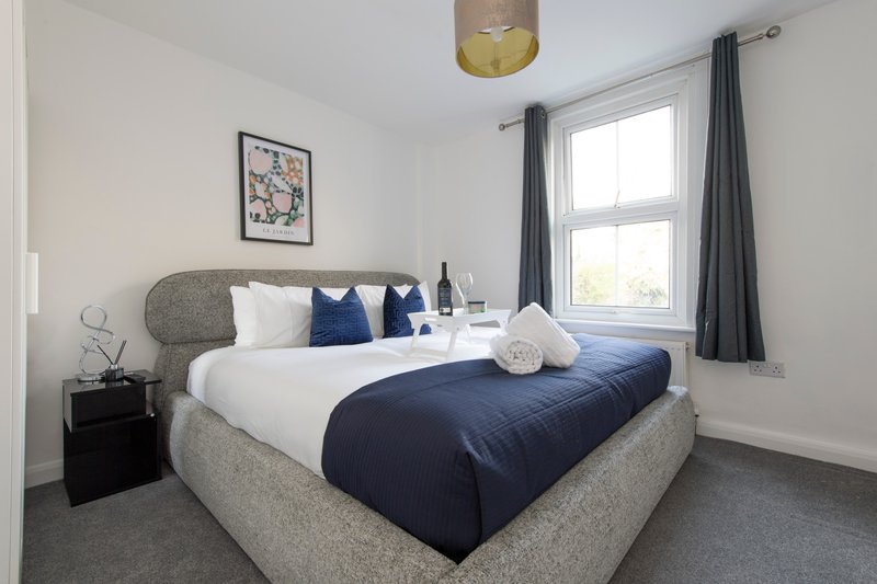 Modern bedroom with grey upholstered bed, navy duvet, white pillows, and window with grey curtains