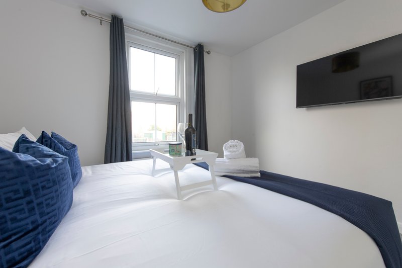 Modern bedroom with double bed, white bedding, blue cushions and armchair by window