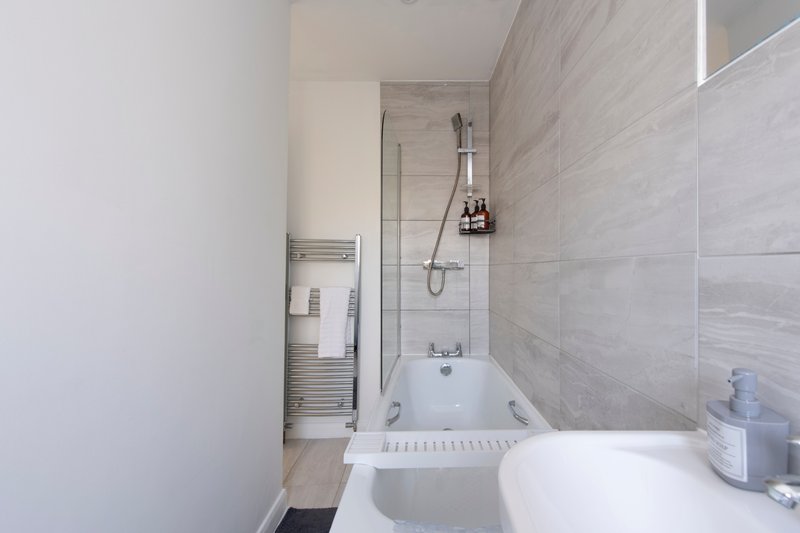 Modern bathroom with white bathtub, grey tile walls, glass shower screen and towel rail