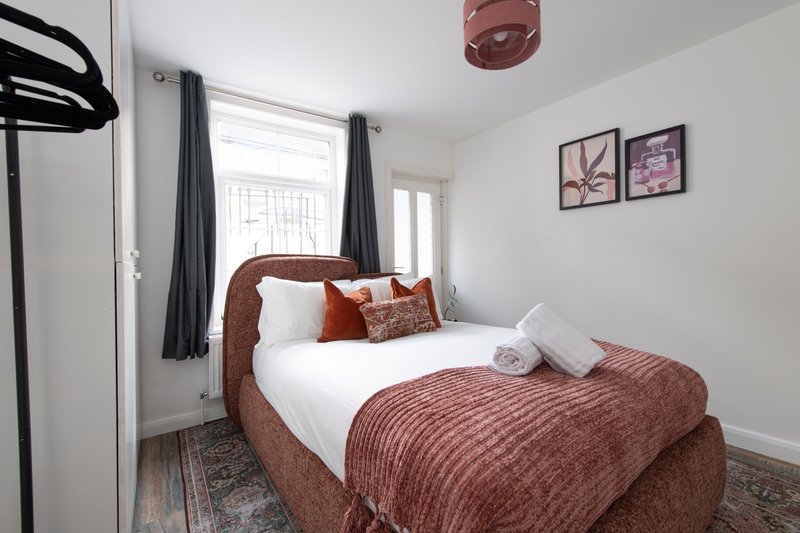 Compact bedroom with burgundy upholstered bed, white pillows, and dark curtains