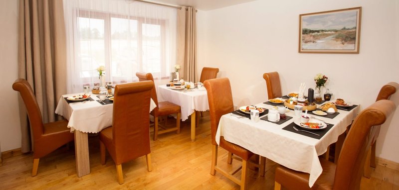 Dining room with wooden floor, set tables with white tablecloths, orange upholstered chairs, and window with curtains