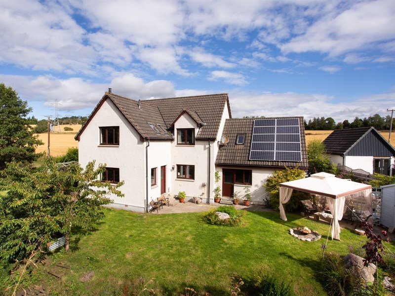 White stone house with dark roof, solar panels, green garden, and rural surroundings