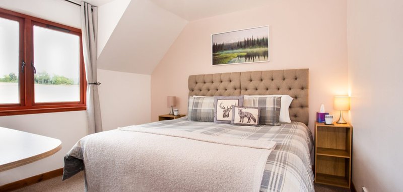 Attic bedroom with double bed, upholstered headboard, wooden furniture and sloped ceiling