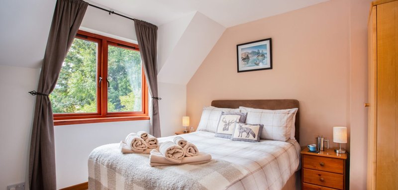 Bedroom with double bed, peach walls, wooden furniture and large window with red frame