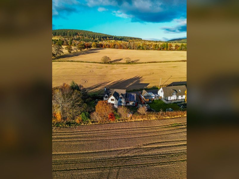 Aerial view of rural property with farmhouse, outbuildings, and surrounding fields and woodland