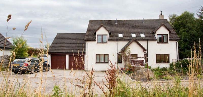 White rendered house with dark roof, driveway, garage and surrounding garden