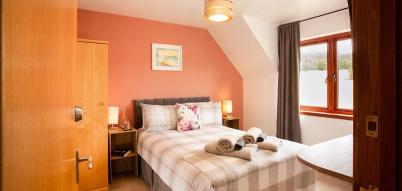 Bright bedroom with double bed, wooden furniture, coral accent wall and window with curtains
