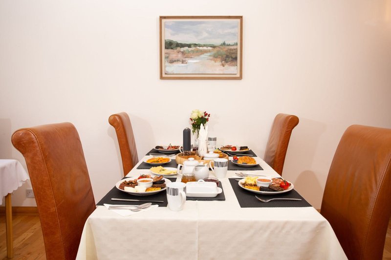 Dining table set for meal with brown leather chairs, framed landscape artwork on wall