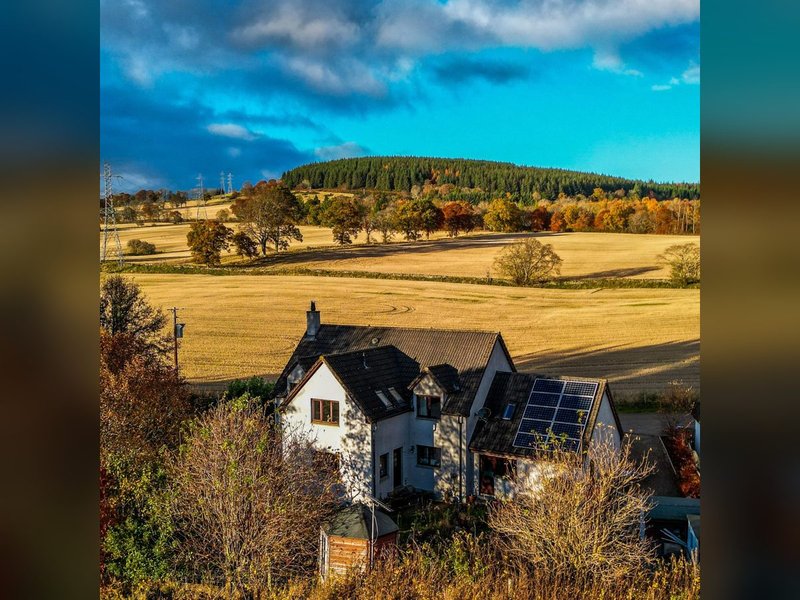 Rural countryside property with solar panels, surrounded by fields and forested hills
