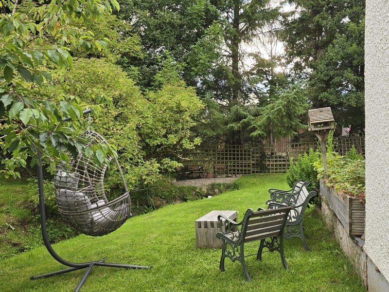 Garden with lawn, seating area, hanging chair and mature trees surrounding property
