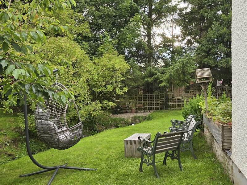 Garden with green lawn, seating area, hammock, and mature trees surrounding property