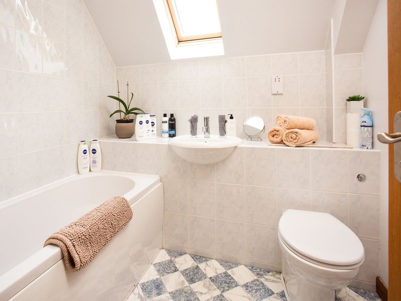 Clean bathroom with bathtub, toilet, sink, skylight and organized toiletries shelf