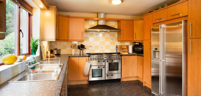 Warm wooden kitchen with stainless steel appliances, granite countertops, and window overlooking garden