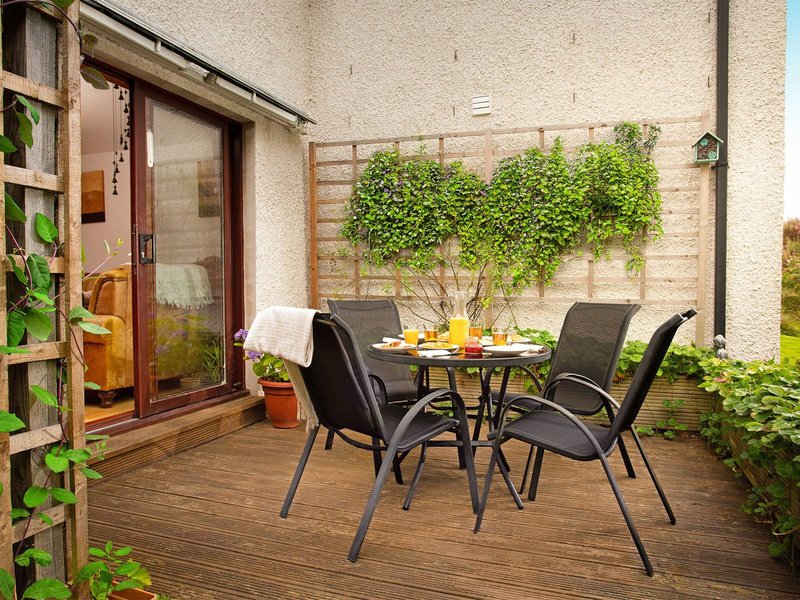 Outdoor patio with wooden decking, black chairs, round table, and climbing ivy on brick wall