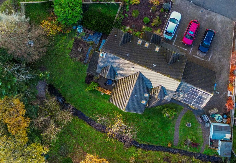 Aerial view of residential property with driveway, parked cars, garden and solar panels